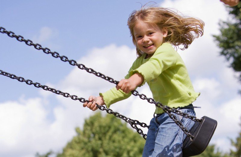 lachend meisje op de schommel in de speeltuin van het vakantiepark